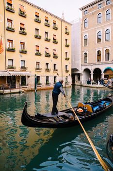 Venice, Italy - 04 october 2019: The gondolier rows a paddle in an empty gondola along the canal, against the backdrop of a yellow five-storey building.