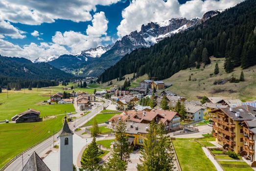 Aerial view of valley with Chalet, green slopes of the mountains of Italy, Trentino, Fontanazzo, huge clouds over a valley, roofs of houses of settlements, green meadows, Dolomites on background,