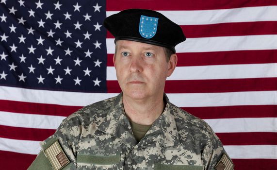 Man wearing military outer shirt and beret with US flag in background