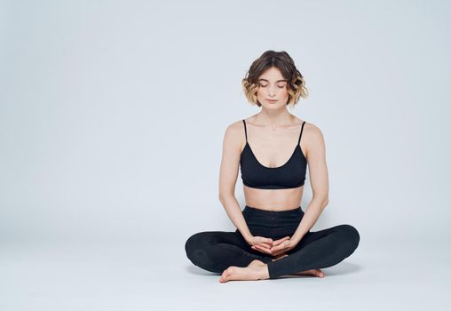 A woman is meditating on a light background with her legs crossed on the floor