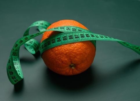 orange wrapped in green measuring tape, slimming concept, cellulite