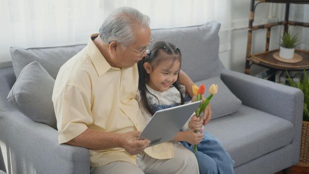 old man looking to tablet computer and granddaughter come visitor at home