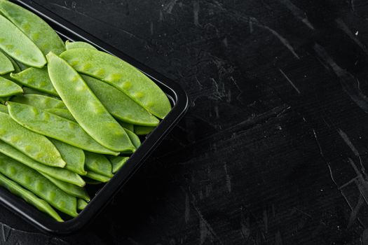 Sugar snap peas, raw ripe baby pods, in plastic container, on black stone background , with copyspace and space for text