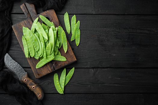 Healthy snap peas, on wooden cutting board, on black wooden background, top view flat lay , with copyspace and space for text