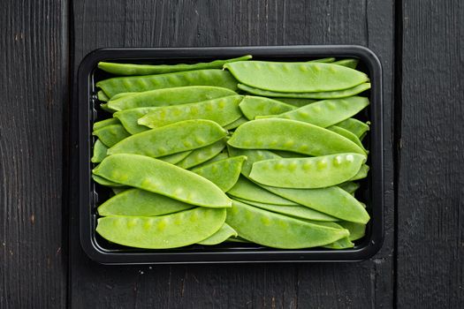 Sugar snap peas, raw ripe baby pods, in plastic container, on black wooden background, top view flat lay