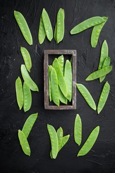 Sugar snap peas, raw ripe baby pods, in wooden box, on black stone background, top view flat lay