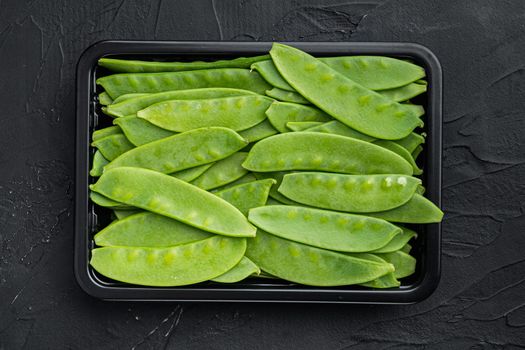 Sugar snap peas, raw ripe baby pods, in plastic container, on black stone background, top view flat lay