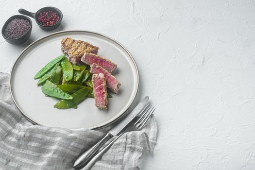 Tuna steak grilled with spring onions and sugar snap peas, on plate, on white stone background , with copyspace and space for text