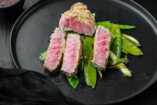 Fried tuna steak in sesame with spring onions and sugar snap peas , on plate, on black stone background