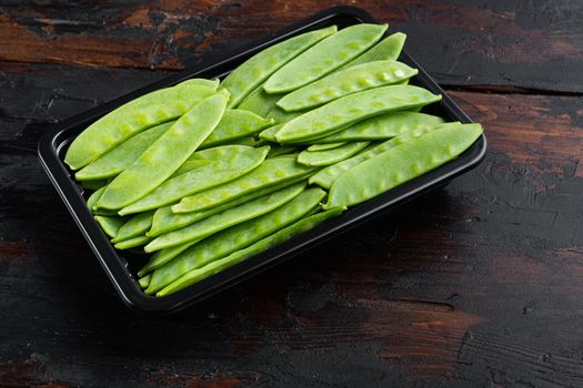 Organic Green Sugar Snap Peas Ready to Eat, in plastic container, on old dark wooden table background