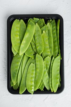 Organic Green Sugar Snap Peas Ready to Eat, in plastic container, on white stone background, top view flat lay