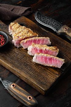 Grilled red rare tuna steak with spring onions and sugar snap peas, on wooden serving board, on old dark wooden table background