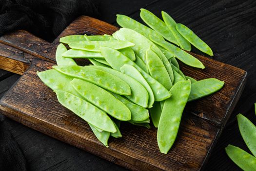 Fresh organic mangetout, also known as sugar snap pea, on wooden cutting board, on black wooden background