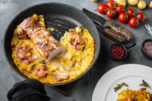 Grilled pork fillet and mash potatoe gratin with sage and prosciutto , on frying cast iron pan and plate, on gray stone background