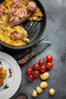 Grilled pork fillet and mash potatoe gratin with sage and prosciutto , on frying cast iron pan and plate, on gray stone background, top view flat lay , with copyspace and space for text