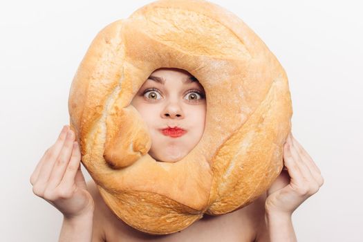 energetic woman grimaces and holds a round loaf of bread in front of her face