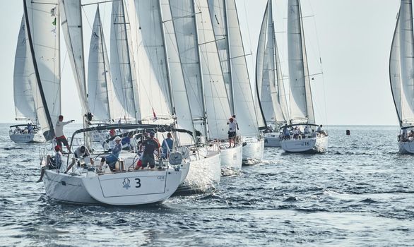 Croatia, Mediterranean Sea, 18 September 2019: Sailboats compete in a sailing regatta, the team turns off the boat, reflection is on water, white sails, boat number aft boats, Strained competition