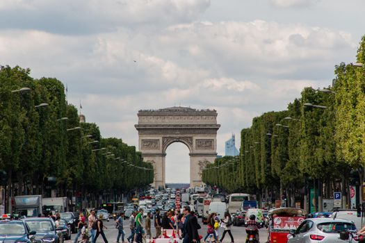 People crossing a congested avenue with French triumphal arch as background