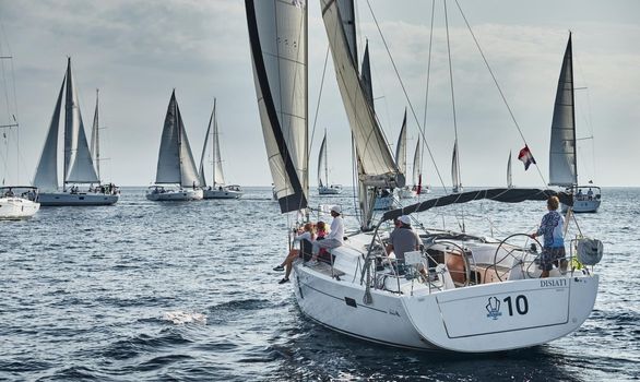 Croatia, Mediterranean Sea, 18 September 2019: Sailboats compete in a sailing regatta, the team turns off the boat, reflection is on water, white sails, boat number aft boats, Strained competition