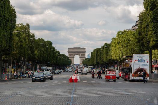 Vehicles passing by in avenue with French triumphal arch as background