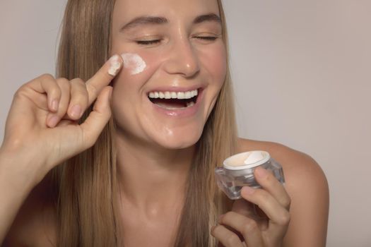 Portrait of a Nice Smiling Girl Laughing and Applying Facial Moisturizer Cream Isolated on Beige Background. Natural Cosmetics. Healthy Lifestyle. Beauty and Skin Care.