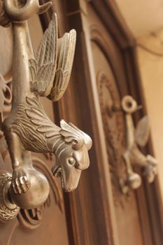 Golden door knocker with mythological dragon shape on old wooden door