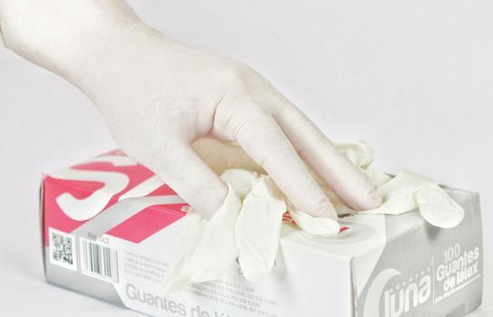 Latex surgical glove box next to hand protected with glove