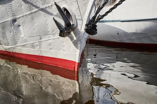 Nasal part of a sailing frigate of white color with an anchor on a nose, bright reflection in water