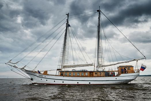 Russia, St.Petersburg, 31 August 2020: Antique sailing frigate of white color to the sea, the lowering storm sky, sails are lowered, masts and ropes