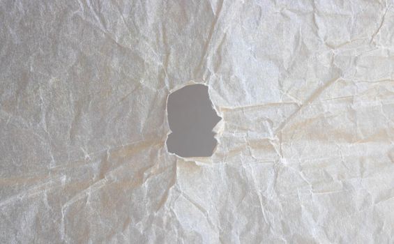 Abstract background of beige crumpled paper with a hole.