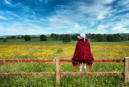 Woman sitting on fence while looking out at the farmland