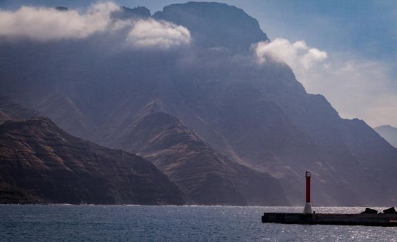 Small beacon in a dock at sea with big mountains in the background