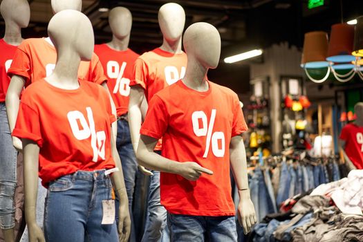 Percentage sign painted on a red t-shirt dressed on a mannequin stands in defocused store