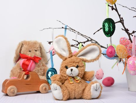 teddy bunny sitting on a white background and decorative colorful easter eggs hang on a branch