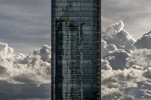 Angular geometric mirror cladding on a modern building with repeating structure and reflected sky and clouds.