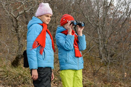 The girl looks with enthusiasm through binoculars, another girl is standing nearby and looks in the same direction