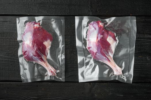 Raw duck leg meat in seal bag for sous vide cooking, on black wooden table background, top view flat lay