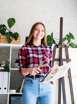 Beautiful woman artist in check shirt painting a picture at home