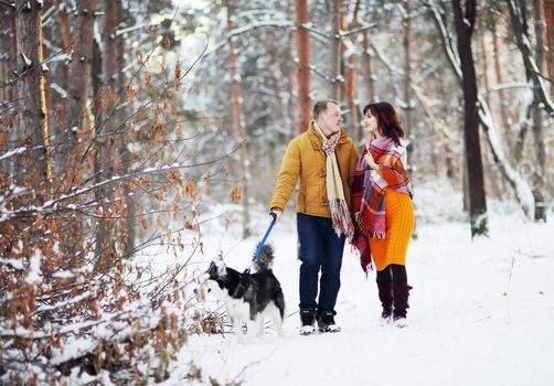 Young couple smiling and having fun in winter park with their husky dog