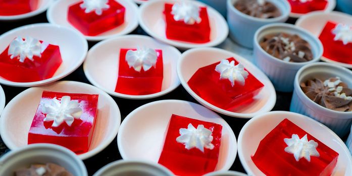 Red jelly dessert with whipped cream served on white plate. Square red jelly in plate on table at restaurant for lunch buffet. Sweet food. Jelly agar. Dessert buffet catering concept, selective focus.
