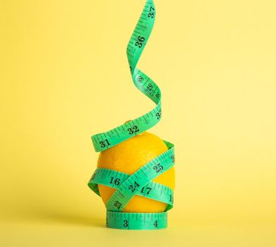 Lemon and tape measure on yellow background. Diet concept.