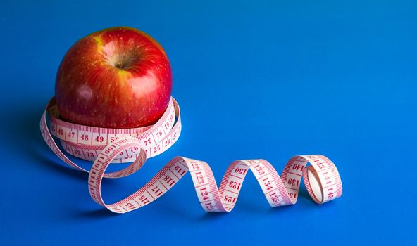 Apple and tape measure on blue background. Diet concept.