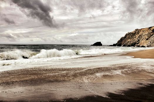 Brave ocean, rock formations and cloudy drama sky on the beach