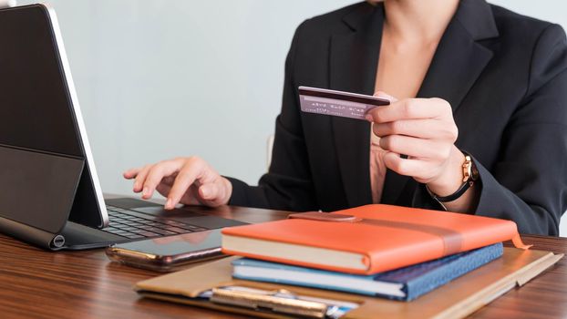 A woman's hand holds a credit card and uses a laptop computer to shop online.On her wooden table.