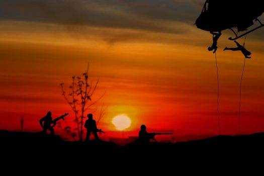 Silhouette Soldiers rappel down to attack from helicopter with warrior beware danger On the ground sunset Background blur and copy space add text ( Concept stop hostilities To peace)