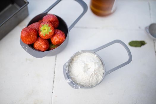 Strawberries and flour in measuring cups above white counter