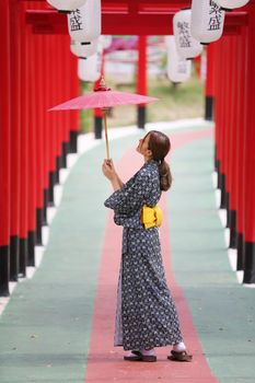 woman in kimono holding umbrella walking into at the shrine red gate, in Japanese garden.