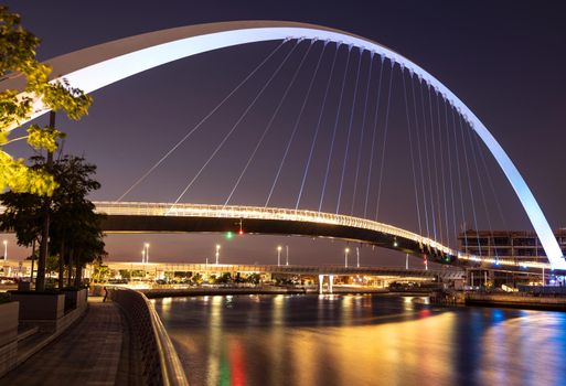 Beautiful view of the illuminated tolerance bridge captured at night time from the Dubai canal boardwalk, Dubai, UAE.