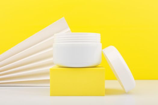 Close up of white opened jar on white table against yellow background decorated with white waver