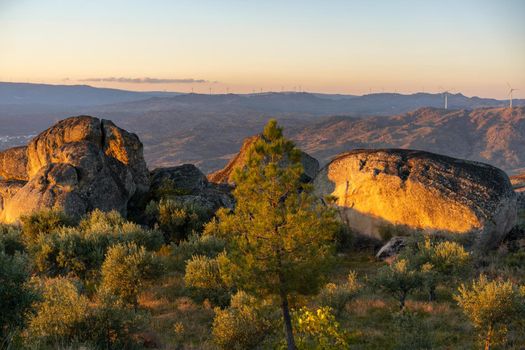 Sortelha nature landscape view with mountains, trees, boulders and wind turbines at sunset, in Portugal